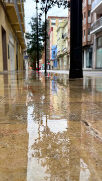 Rain soaked city sidewalk reflecting colorful buildings and streetlights along a quiet urban street after rainfall