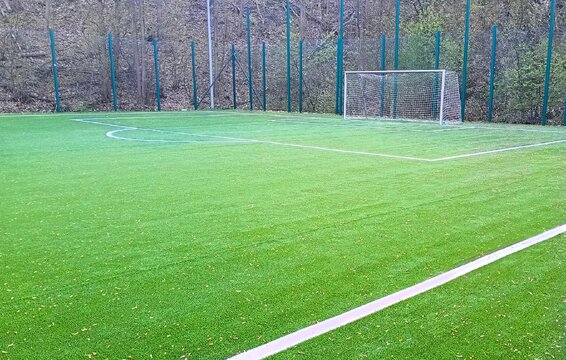 An empty soccer field with a goal and clearly marked turf sits at an outdoor sports ground, illuminated by natural daylight