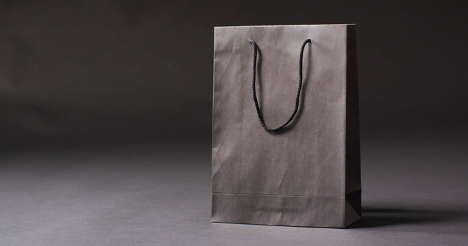 Black gift bag with black handles on dark grey background with copy space