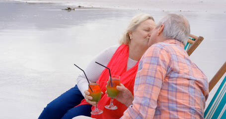 Happy senior caucasian couple sitting in deckchairs kissing and holding cocktails on beach © WavebreakMediaMicro