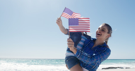 Happy caucasian mother and daughter with flags of usa on beach by sea, copy space © WavebreakMediaMicro