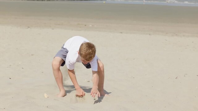 Barefoot boy digging in the sand on a sunny beach slow motion active beach vacation