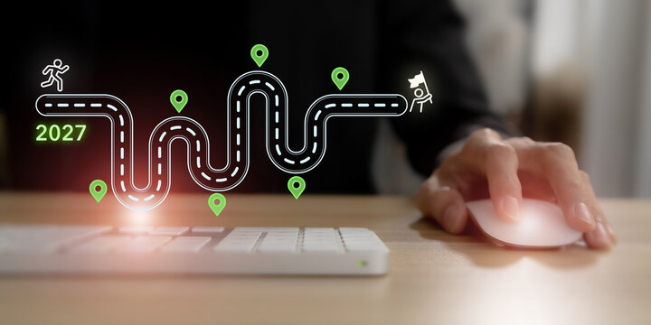 2027 Business Roadmap Concept. Strategic Planning, Milestones, Goal Achievement and Success Journey. Using a computer with virtual 2027 roadmap, winding path, milestone markers and finish flag.