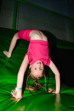 Girl in pink sportswear doing a bridge stretch on a green trampoline safety mat.