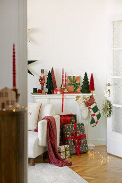 Cozy holiday interior setup featuring a mantelpiece adorned with seasonal ornaments, wrapped presents, stockings, and warm glowing string light