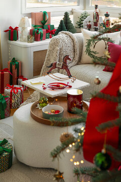 Cozy living room decorated for Christmas with a comfortable sofa, wrapped gift boxes, festive ornaments, and a wooden rocking horse for holiday season joy