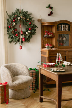 Cozy rustic living room interior decorated for winter holiday celebration with large evergreen wreath, wooden cabinet, comfy armchair, and wrapped gifts present