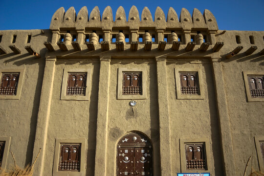 Facade of a traditional mud building with decorated wooden windows and spiky parapet, Mopti Region, Djenne, Mali