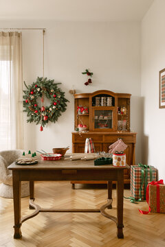Cozy rustic living room interior decorated for winter holiday season with wooden table, festive wreath, traditional cabinet and wrapped presents on floor