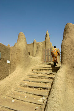 Person in an orange robe climbing the mud staircase leading to the Great Mosque, Mopti Region, Djenne, Mali