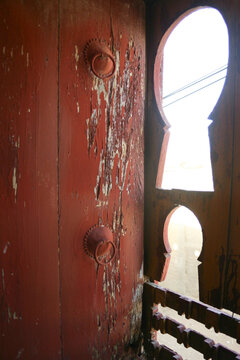 Red wooden shutter with ring handles next to keyhole shaped window openings, Mopti Region, Djenne, Mali