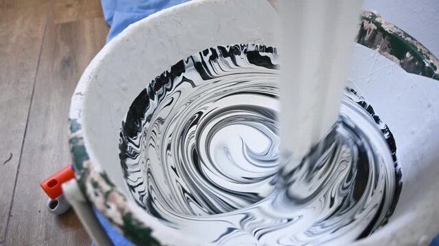 Man kneeling on the floor and mixing white paint in a bucket while preparing to paint an interior wall. DIY home improvement, remodeling and decorating concept.