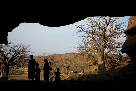 Silhouettes of four children of the Dogon tribe in the mouth of a Tellem burial cave framing baobab trees, Mopti Region, Bandiagara, Mali