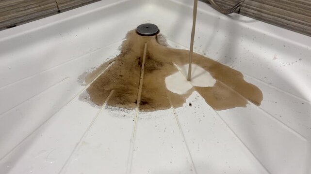 A stream of murky, brown, dirty water pours out, forming a dirty puddle. plumbing problems, clogged drains, bathroom maintenance