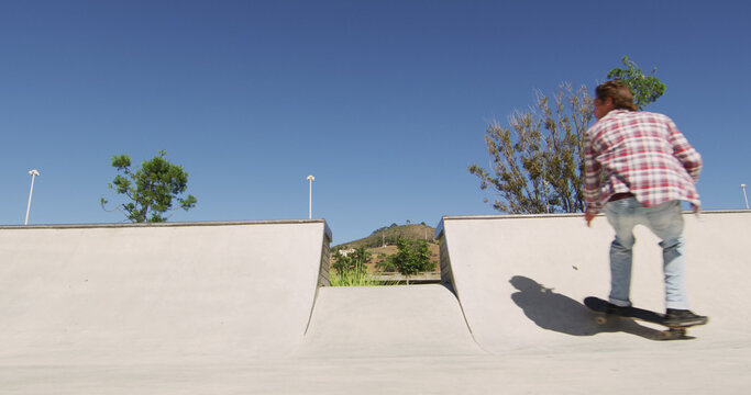 Caucasian man riding and jumping on skateboard on sunny day