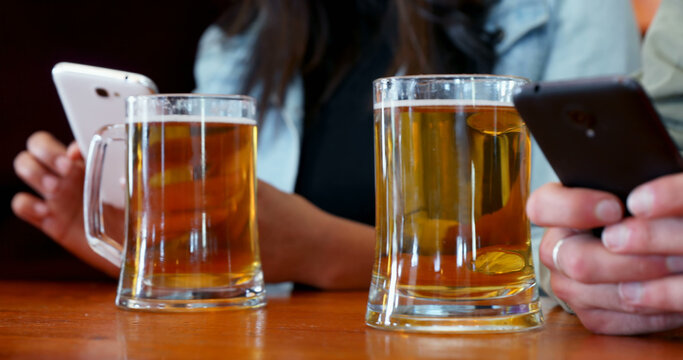 The image depicts a contemporary social setting blending smartphone use with casual drinking.