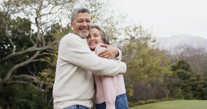 Mature couple embracing, leaning into each other on grassy lawn, wearing knit sweaters and jeans