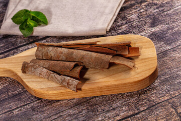 Dried cinnamon bark sticks on wooden cutting board with linen napkin and fresh mint leaves on rustic dark wood table, natural spice ingredient still life © Andrei Starostin