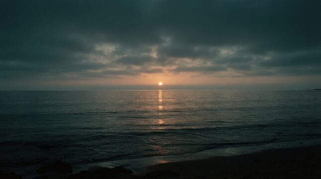 Small glowing sun reflected across calm dark water beneath hazy clouds, minimalist seascape photography, teal, amber and charcoal palette, soft atmospheric light, tranquil cinematic evening mood.