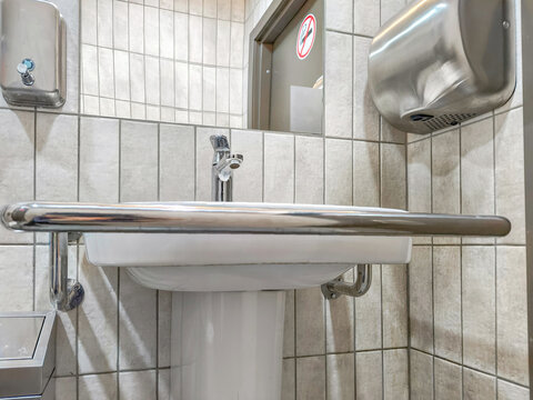 Accessible bathroom sink with grab bar and tiled walls. Public restroom hygiene and universal design. Barrier free facilities for mobility access. Sanitation and inclusive infrastructure