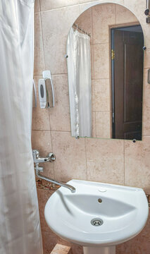 Bathroom sink with mirror and shower curtain in tiled washroom. Compact bathroom interior. Personal hygiene and daily washing routine. Household plumbing and sanitation