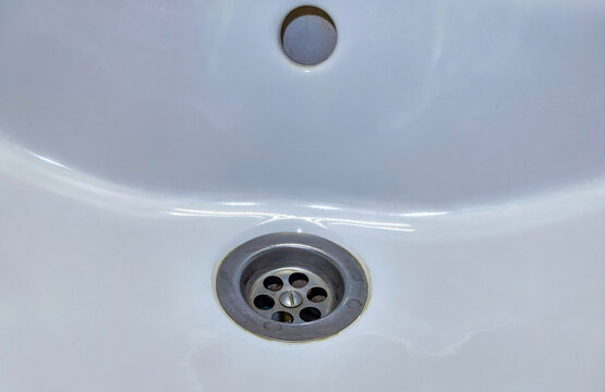 Close-up of metal drain in white bathroom sink. Plumbing fixture for everyday handwashing and personal hygiene. Household maintenance and bathroom cleaning concept