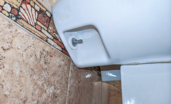 Close up of ceramic sink with exposed mounting bolt beside patterned bathroom tiles. Plumbing repair and fixture maintenance. Bathroom sanitation and home improvement concept