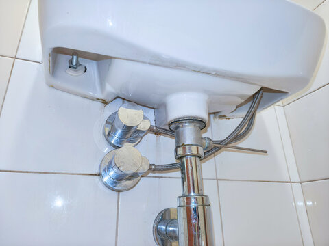 Close-up of plumbing beneath a bathroom sink with exposed pipes, valves and fittings. Sink repair and maintenance. Household plumbing inspection and renovation