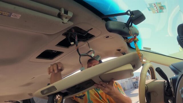 Man fitting the interior overhead console panel back into the roof of a camper van after insulation work during a DIY conversion project.
