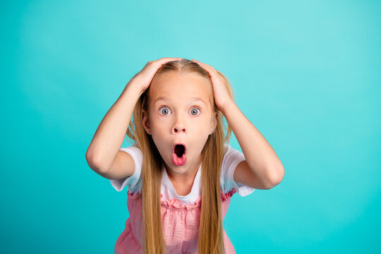 Surprised young girl with hands on head and wide open mouth looking shocked against turquoise background