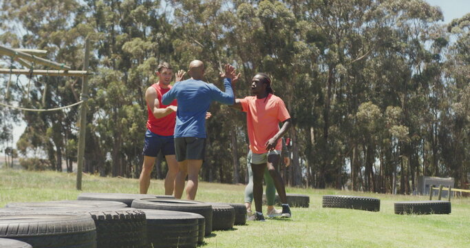 Diverse fit group running through tyres and high fiving in the sun at obstacle course