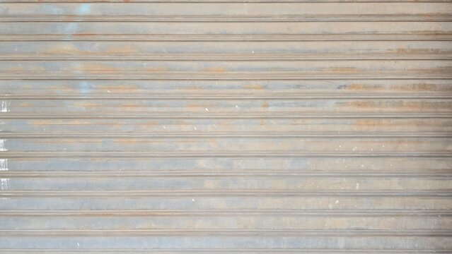 Old dusty metal roller shutter door with stains texture. Grunge rusty metallic rolling gate backdrop background. Abstract horizontal lines pattern on dirty rusty metal door.