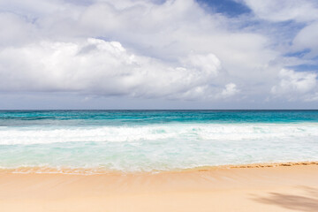 A tranquil ocean beach scene with turquoise water, wet sand, and gentle waves under a dramatic, cloud-filled sky. Ideal for travel, vacation, and relaxation themes. Seychelles © evannovostro