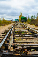 Railway background - converging rusty tracks, wooden sleepers and a green locomotive with a freight car in the distance under a cloudy sky © syntheticmessiah