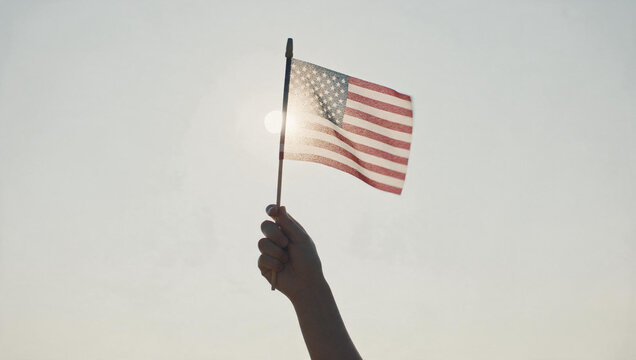 Hand Holding American Flag Against Bright Sunny Sky