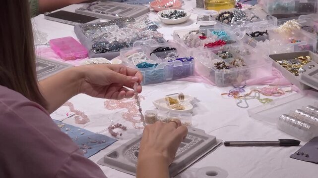 Woman assembling beaded bracelet at craft table, wide shot. Handmade jewelry design, creative workshop. Creative hobby.