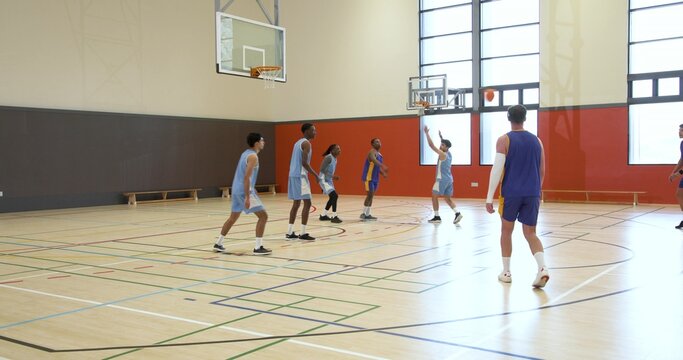 Male basketball players shooting jump shot and defending on gym court with hoop, copy space