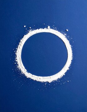Ring of fine white powder on deep blue paper, minimal overhead flat lay with copy space