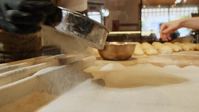 Baker uses fine metal sieve to sift delicate white flour over linen couche. Worker prepares surface for freshly shaped baguette dough. Slow motion