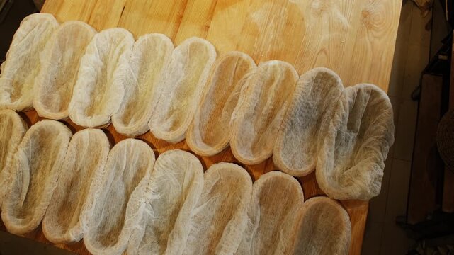 Baker arranges rattan proofing baskets across wooden table. Bakery worker uses natural containers as convenient supports for soft elastic dough