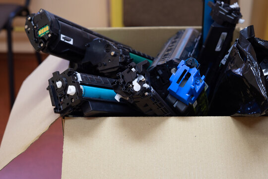 Collection of used printer toner cartridges in a cardboard box prepared for recycling and responsible electronic waste management.