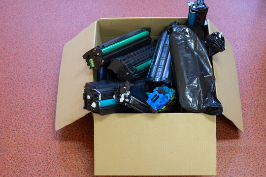 Collection of used printer toner cartridges in a cardboard box prepared for recycling and responsible electronic waste management.