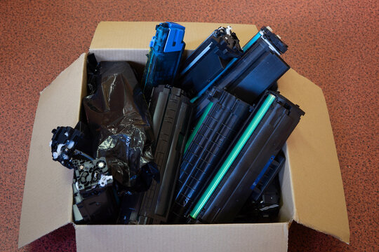 Collection of used printer toner cartridges in a cardboard box prepared for recycling and responsible electronic waste management.