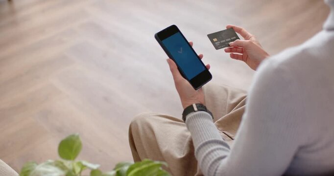 Seated adult is aligning card with phone in home as app is loading, checkmark confirming payment