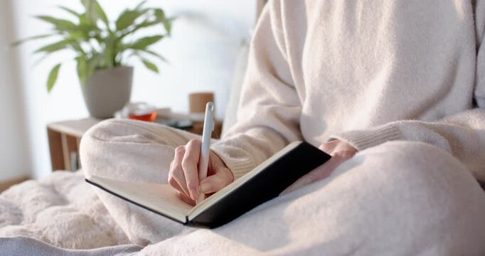 Touching pen to page is initiating person writing in black notebook on plush blanket for journaling