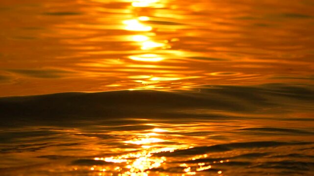 Fiery ripples wash against dark sand as the evening sun descends, casting warm reflections across the surface. Low angle static close-up shot.