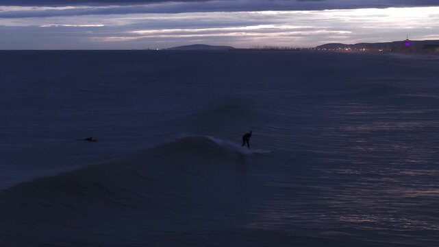 Surfers on waves with Carnon lights in the distance