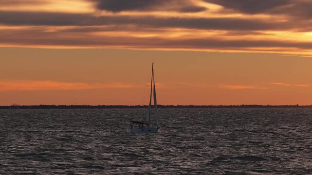 Sailboat silhouette on sea under orange sunset near Carnon