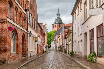 Lüneburg, Germany - Historic street in the old town with traditional brick Gothic architecture, colorful medieval houses, wet cobblestones and a church tower under an overcast sky © bbsferrari