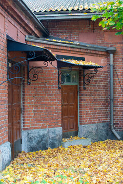 Old red brick building with wooden doors in Helsinki, wrought iron canopies and fallen yellow autumn leaves